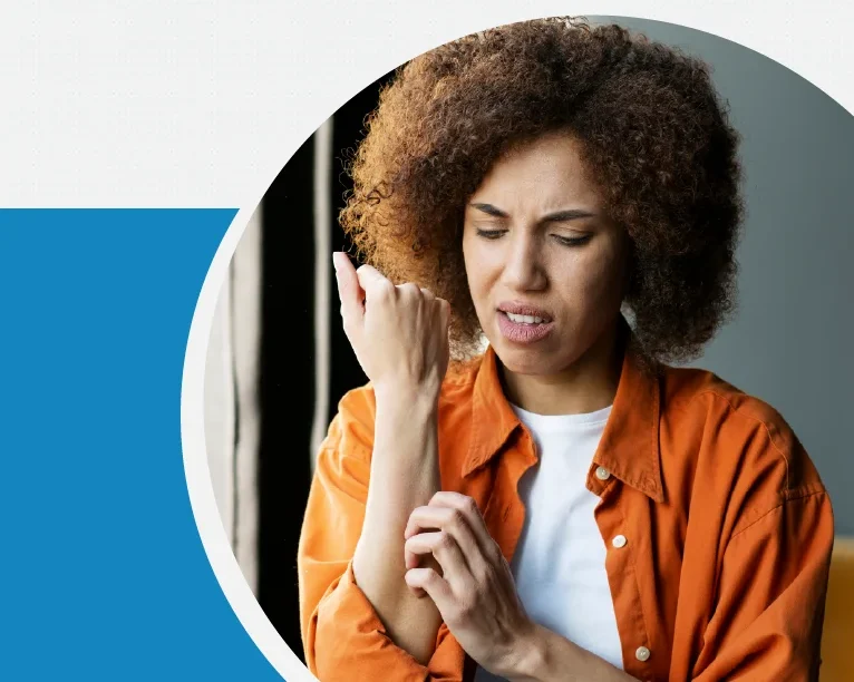 Curly-haired woman in an orange shirt looks distressed while examining her wrist for pain