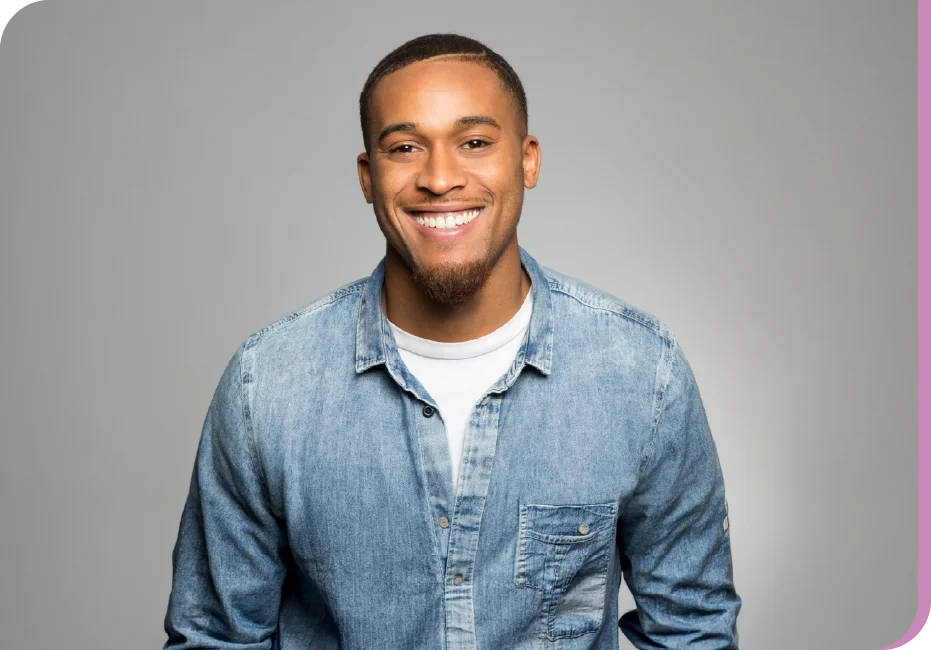 Smiling man in a light denim shirt posing for a portrait against a gray backdrop.
