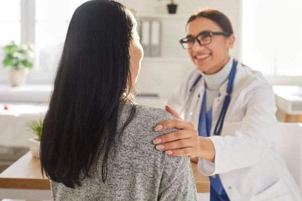 Female doctor with a stethoscope reassures a patient in a bright clinic, placing a comforting hand on her shoulder